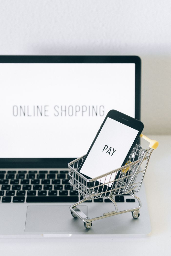 A smartphone placed in a small cart on top of a laptop represents online shopping and digital payment.